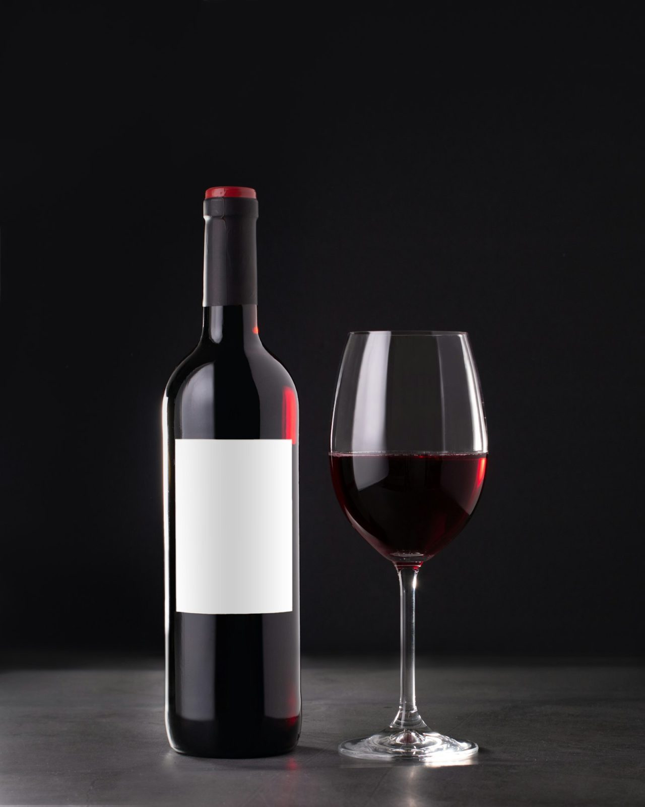 single-red-wine-bottle-with-blank-label-for-mockup-and-glass-of-red-wine-on-dark-gray-background